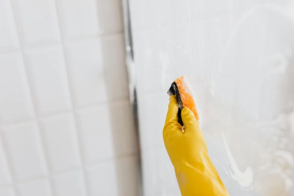 Close-up of hand cleaning window with squeegee outdoors using yellow gloves.